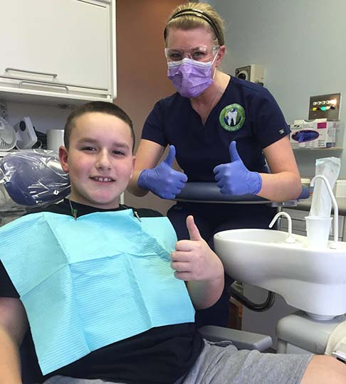 Smiling boy in dentist chair with thumbs up gesture.