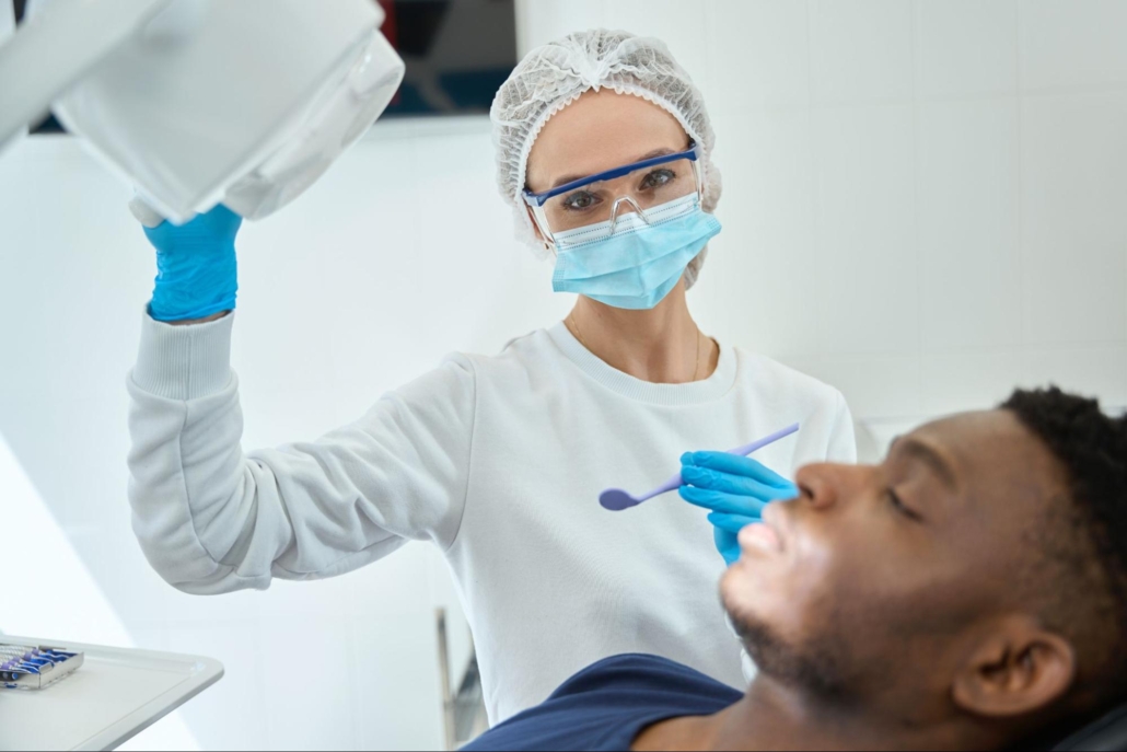 Female dentist next to a male patient who has his eyes closed. 
