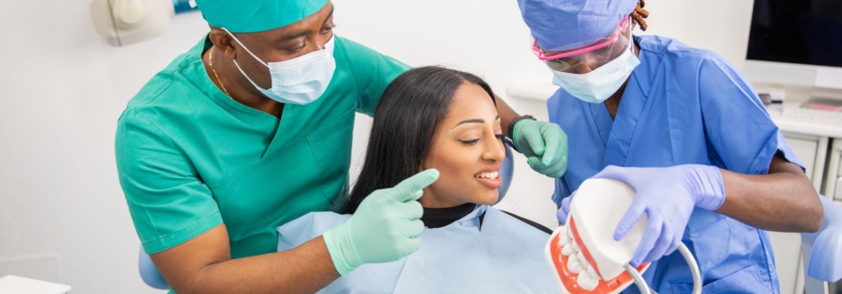 A dental patient next to two professionals in a dental exam room.