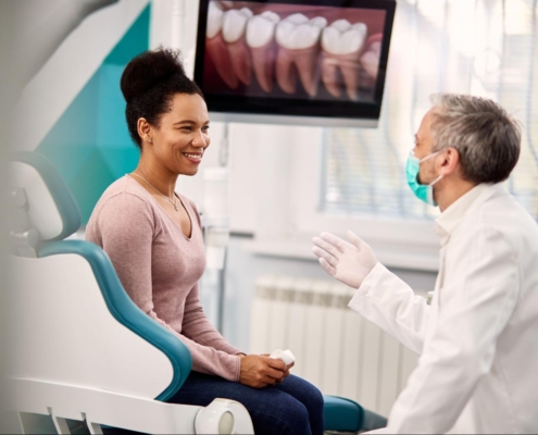 A female patient in a dental office having a conversation with the dentist while an x-ray is on a screen behind them.