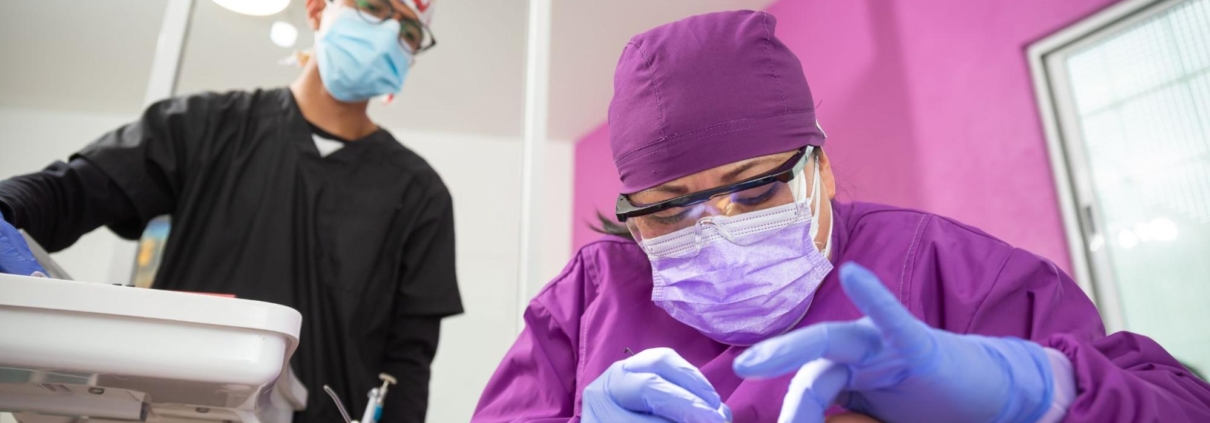 A female dentist in purple scrubs performing a dental procedure on a patient with her assistant.