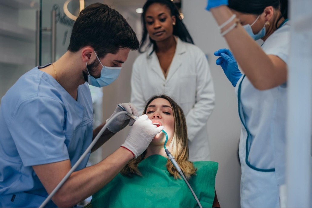 Woman surrounded by a dentist and two hygienists in an exam room. 