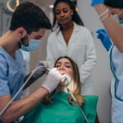 A doctor and two dental assistants performing a procedure with a woman wearing a green shirt.