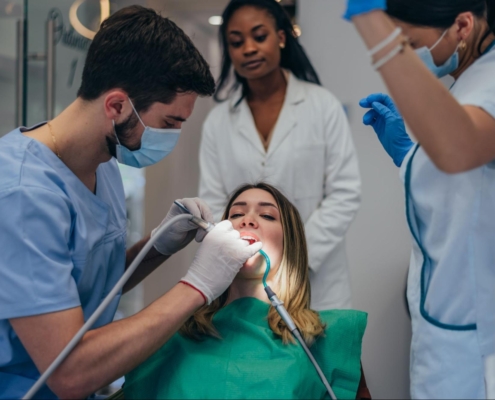A doctor and two dental assistants performing a procedure with a woman wearing a green shirt.