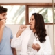 A couple looking at each other while brushing their teeth.