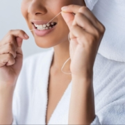 Cropped view of a woman wearing a bathrobe and smiling while flossing her teeth in the bathroom.