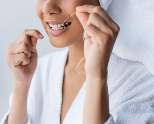 Cropped view of a woman wearing a bathrobe and smiling while flossing her teeth in the bathroom.